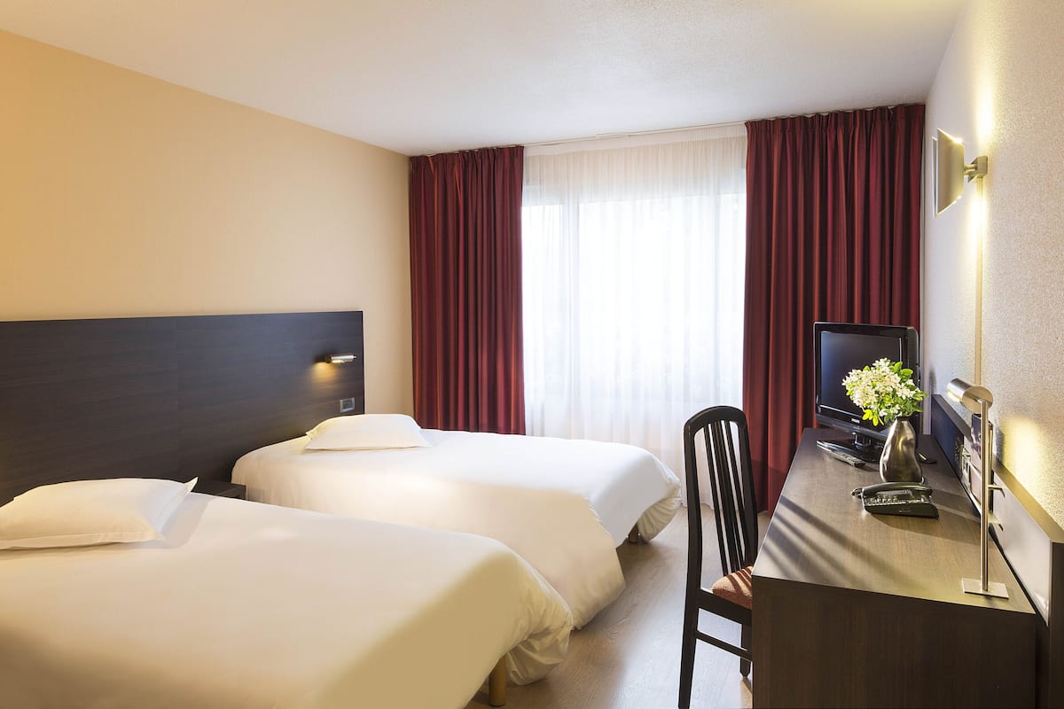 A hotel room with two beds, a desk with a computer, and a TV.