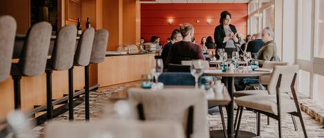 A modern restaurant with wooden paneling and a red accent wall. Tables are set with wine glasses and plates.