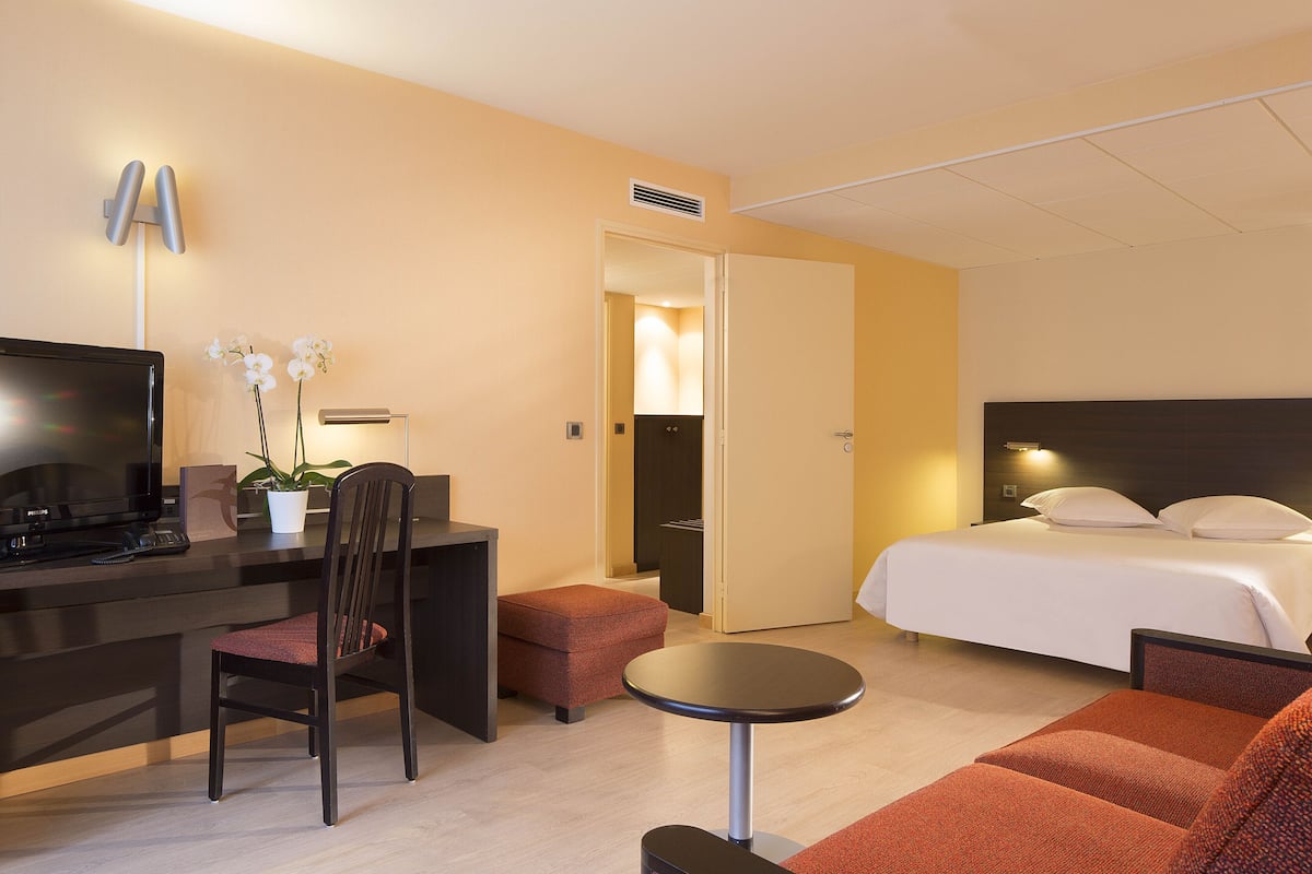 A hotel room with a bed, a desk with a computer, a chair, a small table, and a sofa.