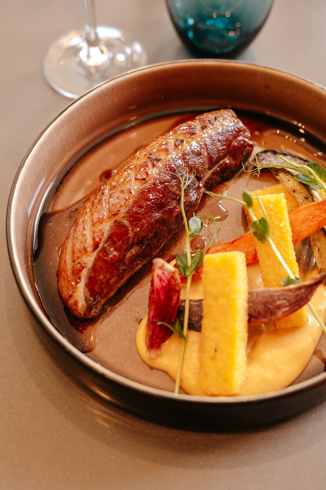 Un plato con un guiso de carne, adornado con hierbas y verduras, sobre una mesa.