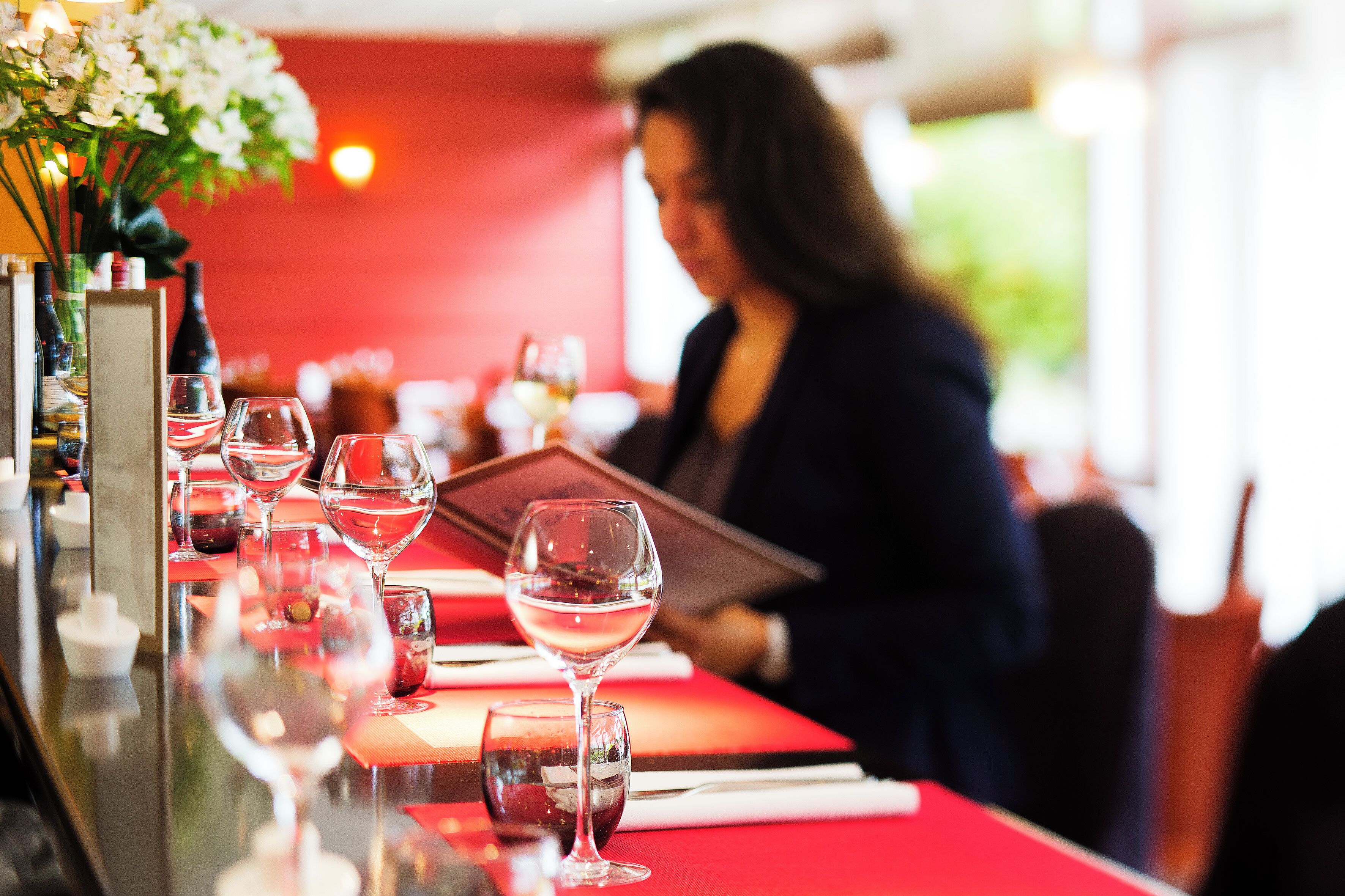 A restaurant setting with a red tablecloth, wine glasses, and a menu.