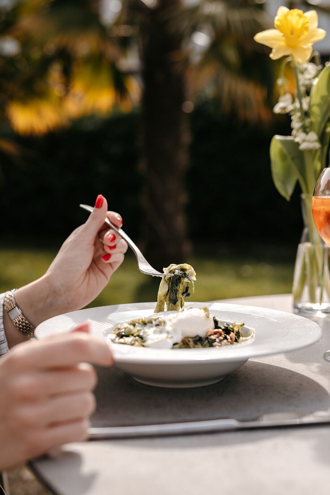 Une personne est assise à une table, mangeant en plein air, avec une assiette de nourriture, une fourchette et un verre à portée de main.