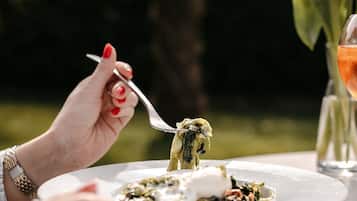 Une personne est assise à une table, mangeant en plein air, avec une assiette de nourriture, une fourchette et un verre à portée de main.