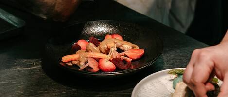 Una persona cocinando en una cocina, con una sartén en la hornilla y un plato de comida sobre la encimera.