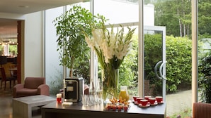 Un salón moderno con un ventanal grande, una cafetera y una zona de comedor visible a través del ventanal.