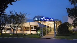 Una entrada de hotel con un vestíbulo cubierto, fachada de vidrio y un letrero que dice 'Escale Oceania'.