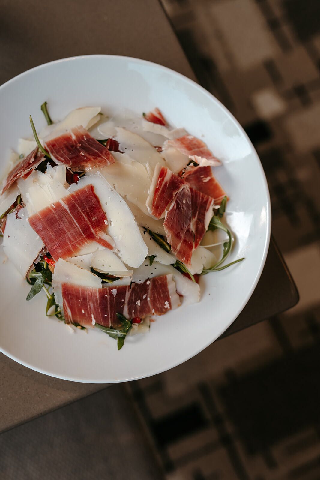 A plate with thinly sliced prosciutto and arugula.