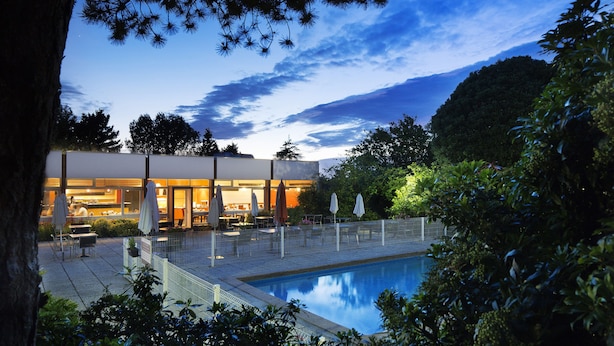 Zona junto a la piscina con mobiliario exterior y un edificio al fondo.