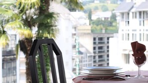 Una mesa servida con platos, una copa de vino y una servilleta, con vistas a edificios y una palmera al exterior.