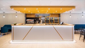 Un área de bar moderna con mostrador de madera, asientos y una variedad de botellas y vasos en estantes.