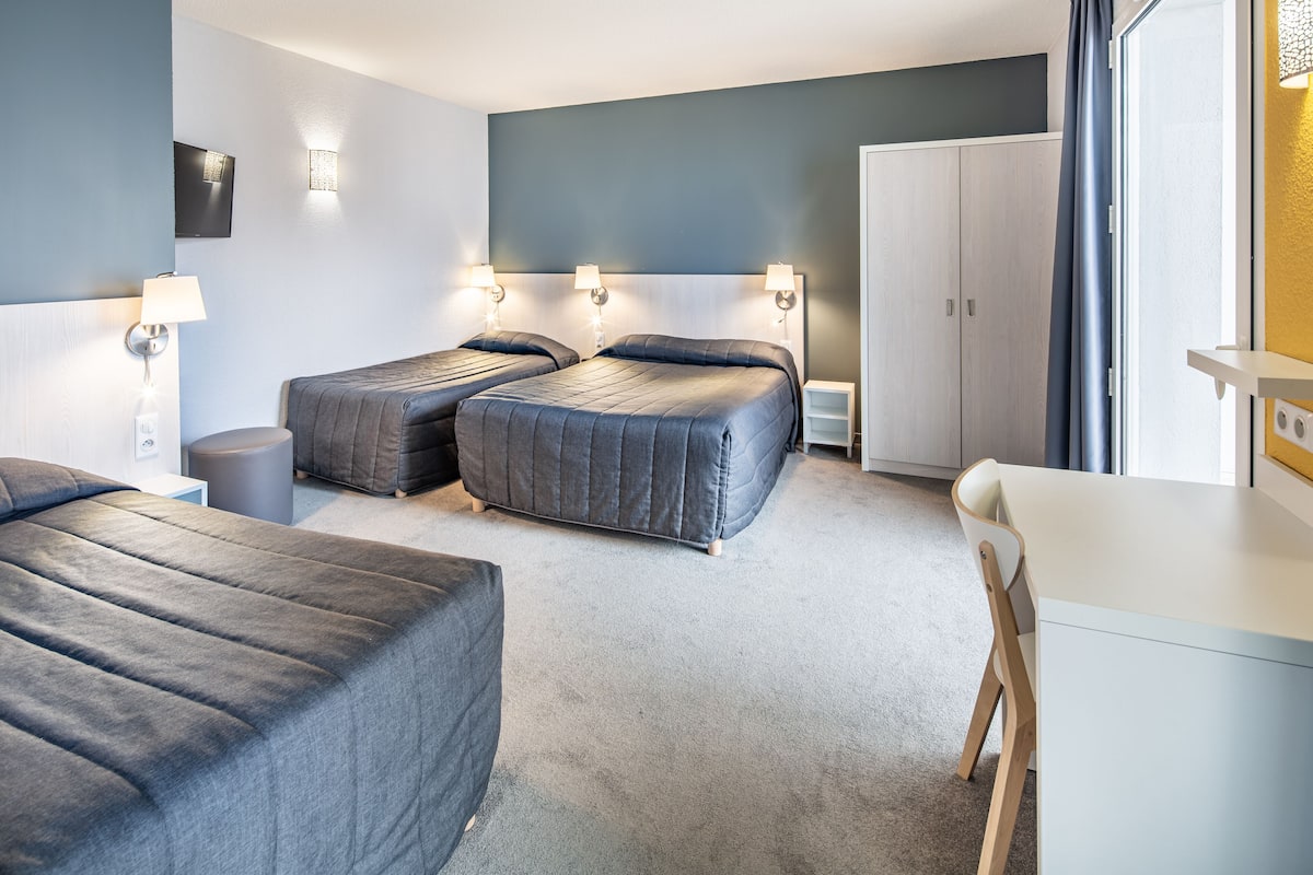 Ein Hotelzimmer mit zwei Betten, einem Schreibtisch, einem Stuhl, einem Kleiderschrank und einem an der Wand befestigten Fernseher.