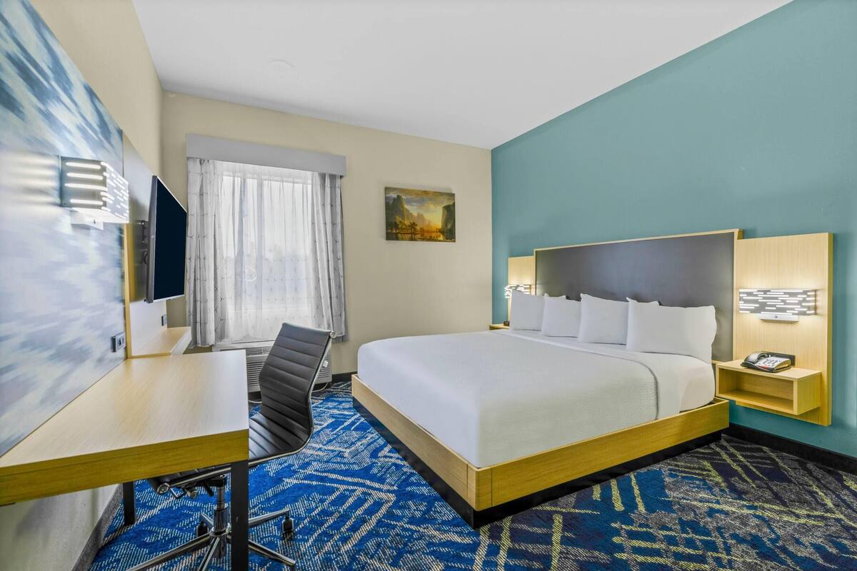 A hotel room with a large bed, a desk, a chair, a TV, and a painting on the wall.