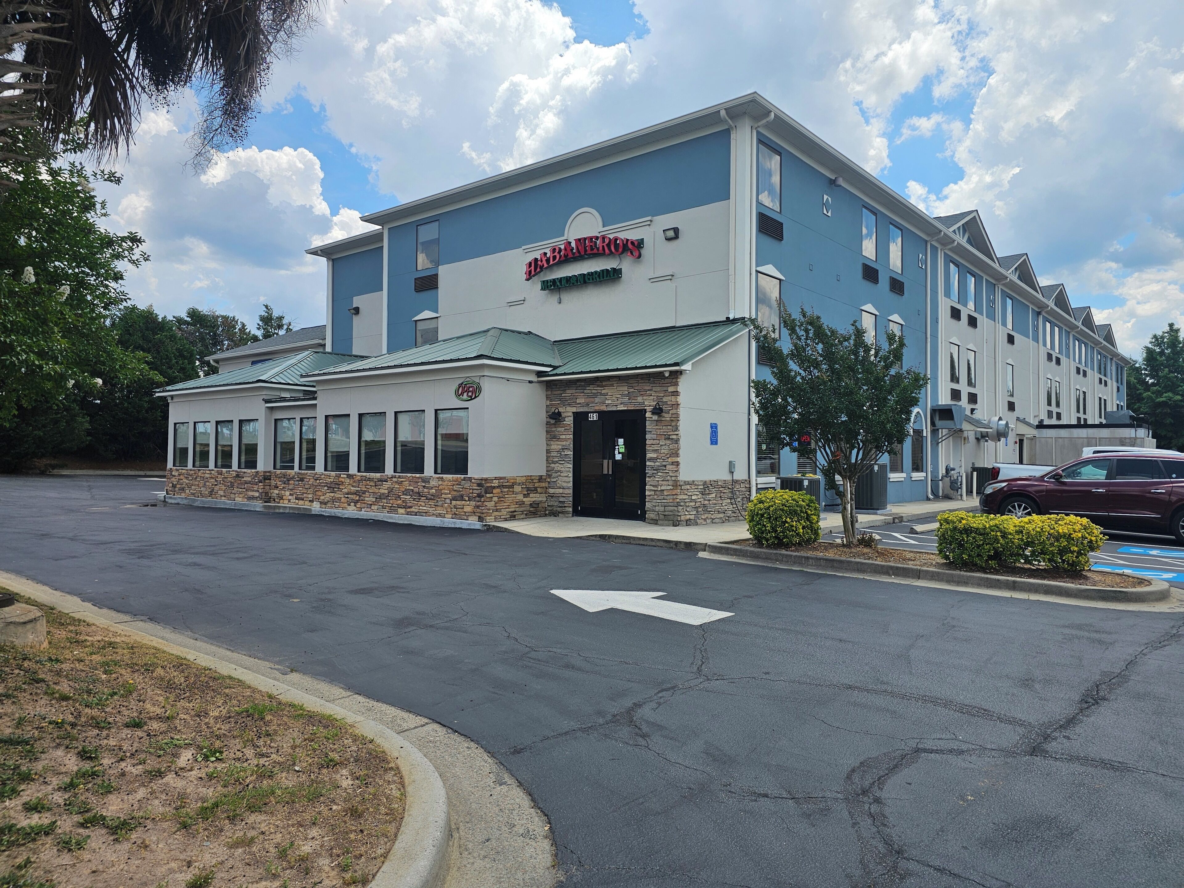 A hotel with a blue and white exterior, a sign reading 'Habaneros Mexican Restaurant,' and a parking lot with a maroon car.
