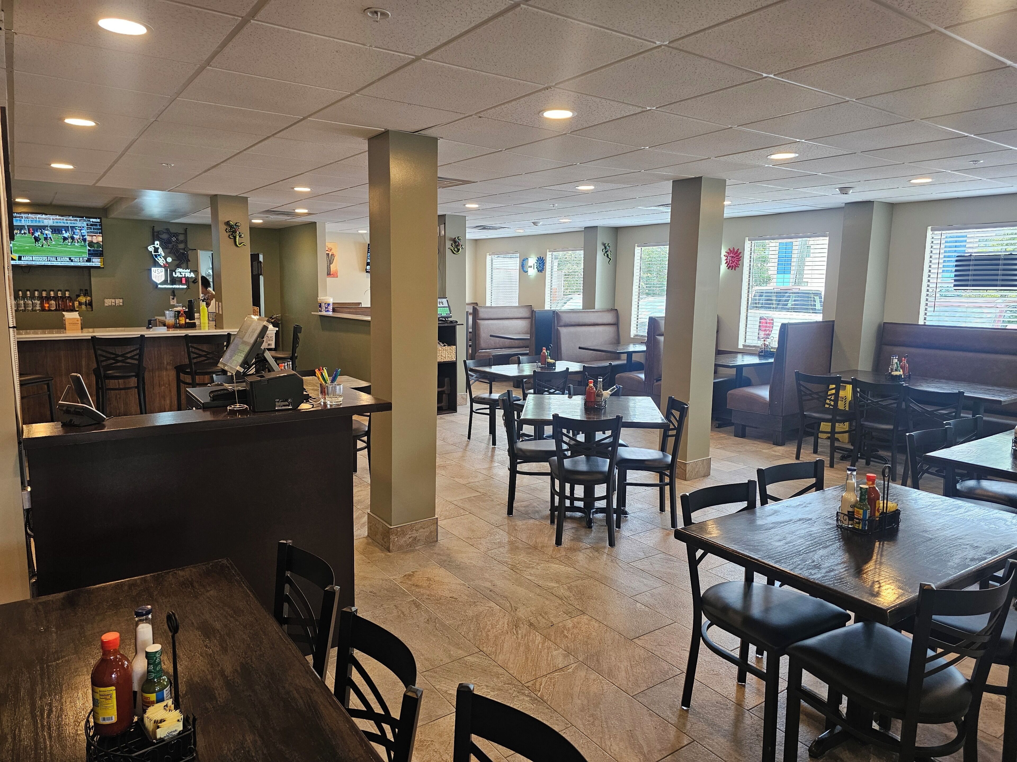 L’intérieur d’un restaurant avec des banquettes, des tables, un bar et un écran de télévision pour diffuser des événements sportifs.