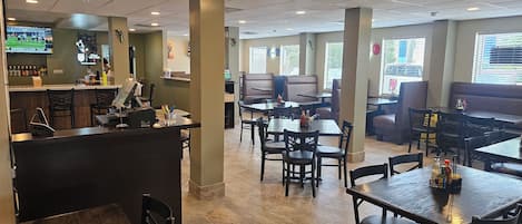 L’intérieur d’un restaurant avec des banquettes, des tables, un bar et un écran de télévision pour diffuser des événements sportifs.