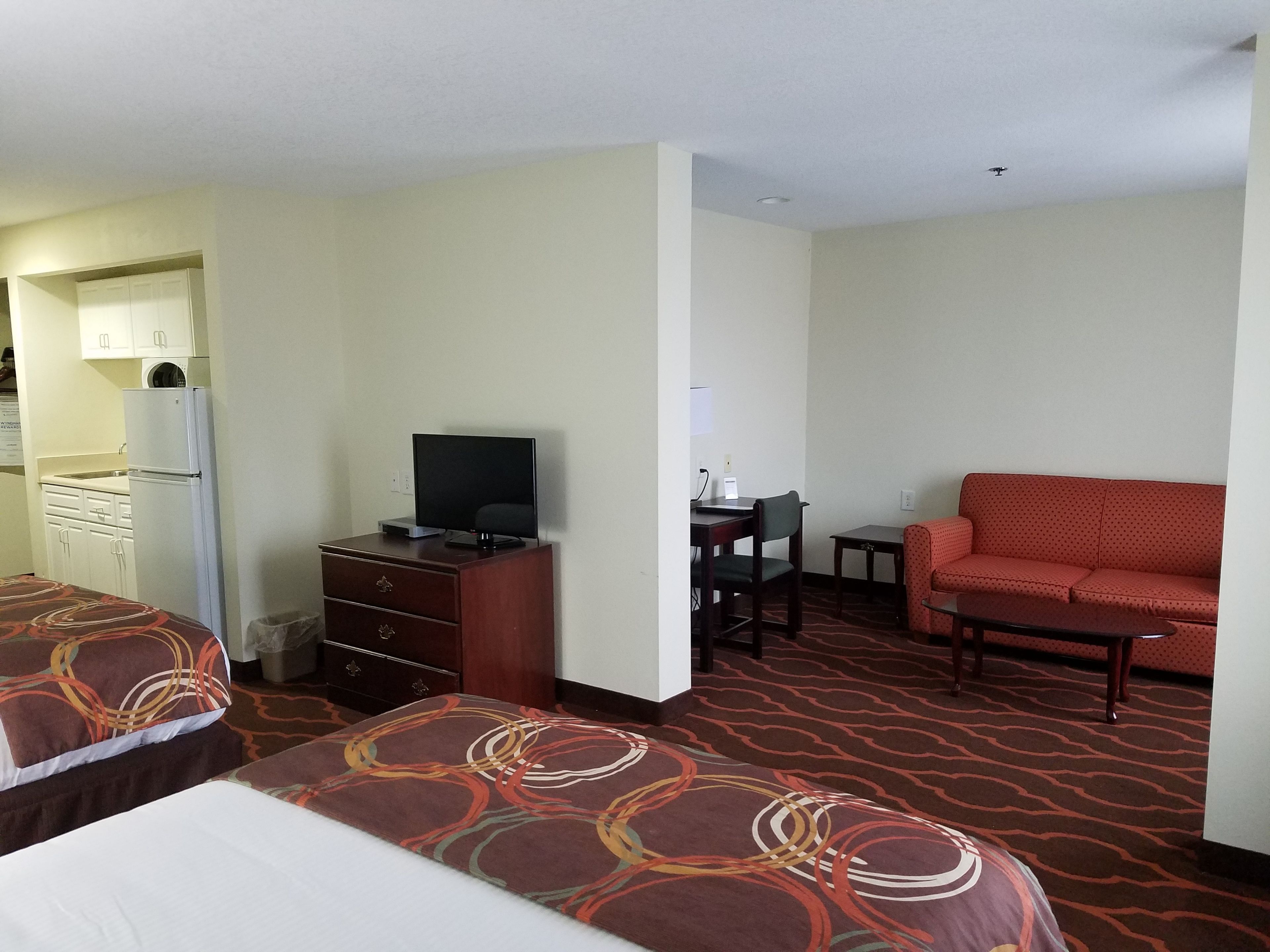 A hotel room with two beds, a TV, a desk, a chair, a sofa, and a kitchenette.
