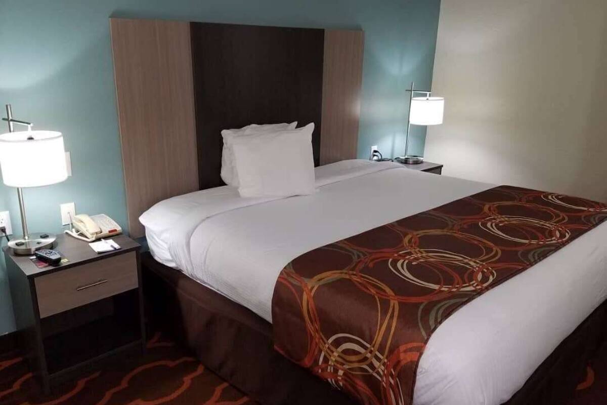 A hotel room with a bed, a nightstand with a phone and lamp, and a headboard.
