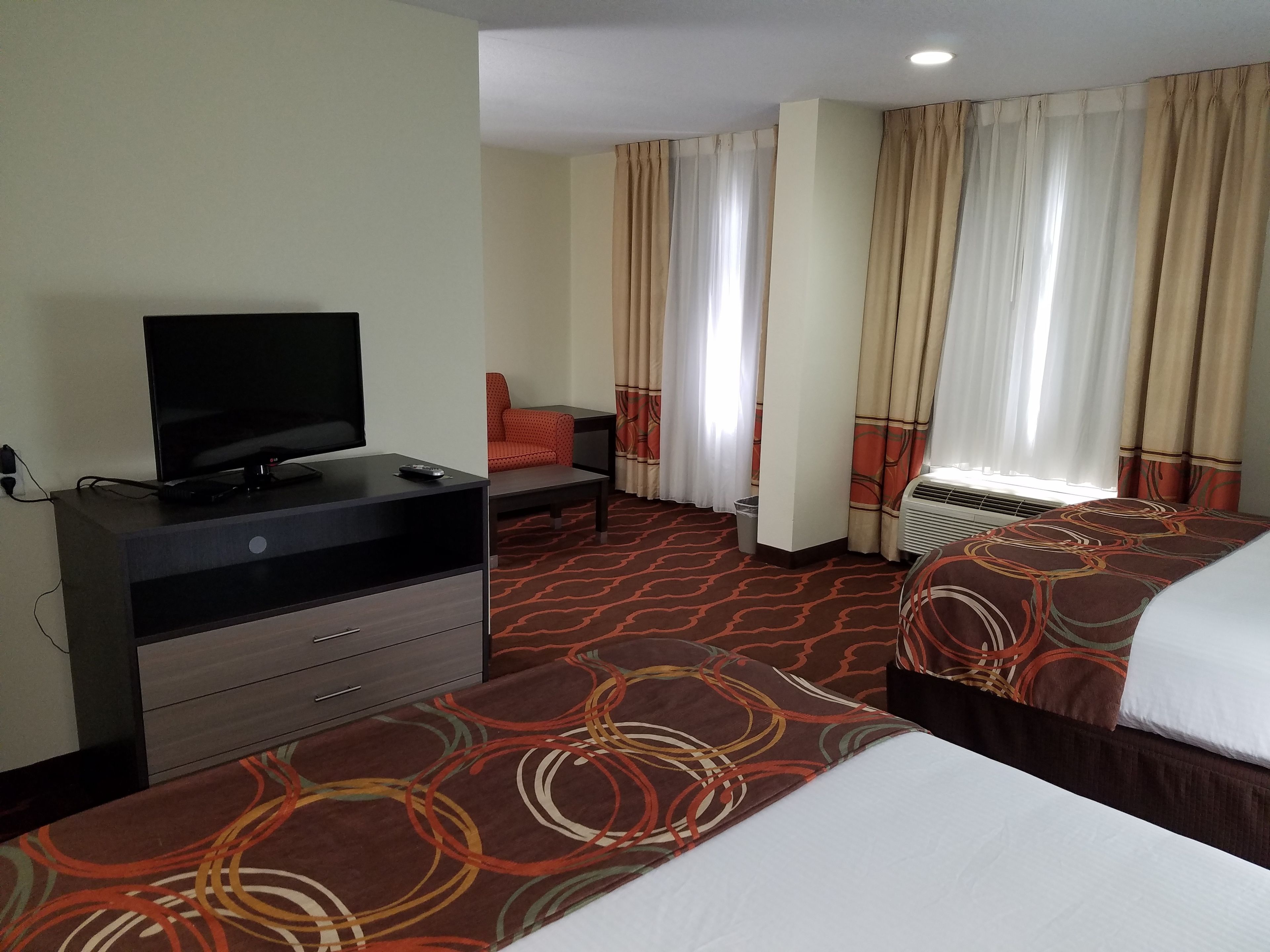 Habitación de hotel con una televisión sobre un tocador, dos camas con cubrecamas estampados, una silla y un ventanal con cortinas.
