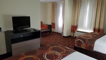 A hotel room with a TV on a dresser, two beds with patterned bedspreads, a chair, and a window with curtains.