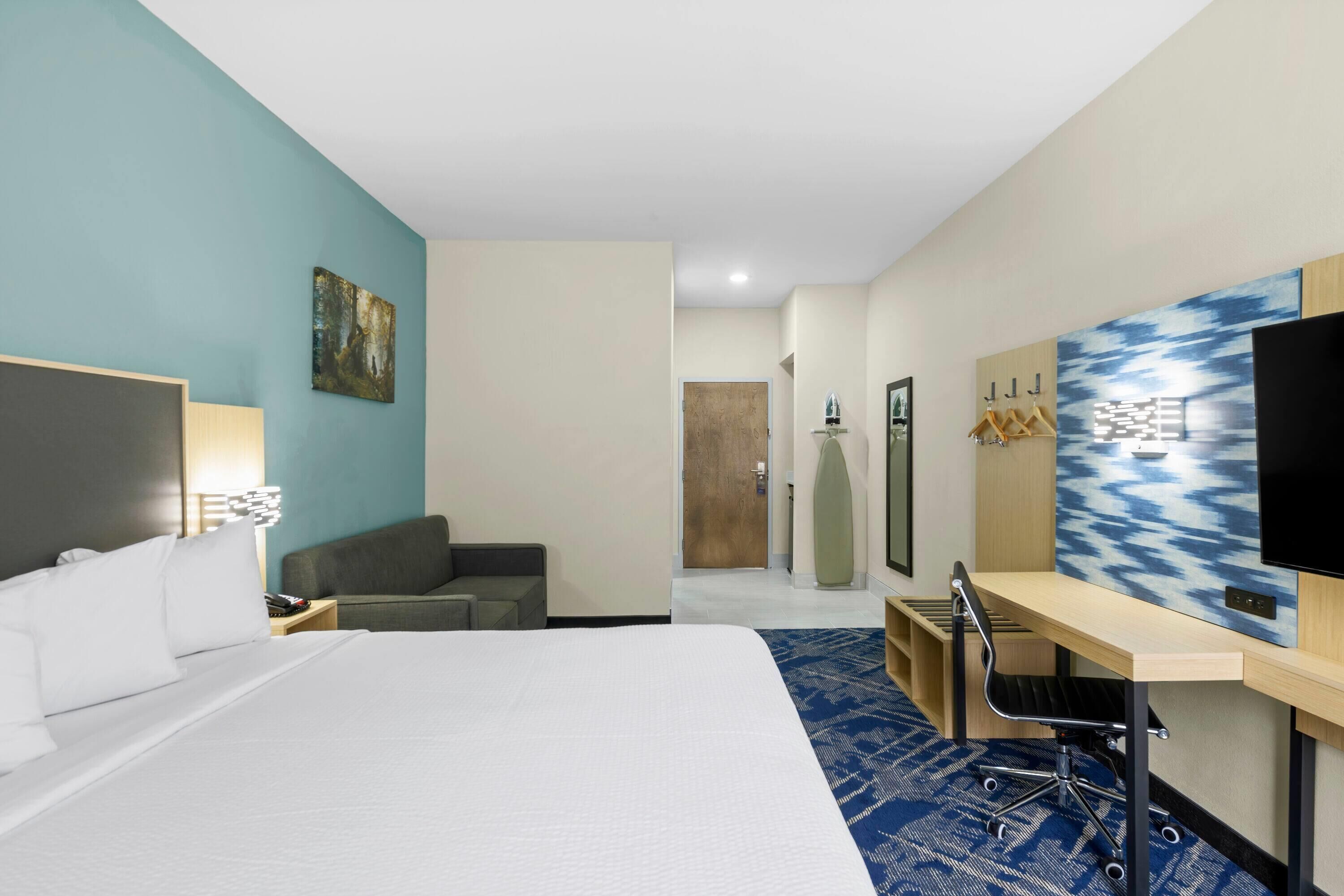 Habitación de hotel con una cama grande, un escritorio con silla, un televisor y un cuadro en la pared.