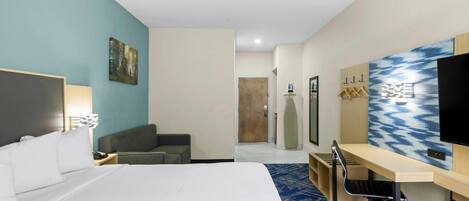 Ein Hotelzimmer mit einem großen Bett, einem Schreibtisch mit Stuhl, einem Fernseher und einem Bild an der Wand.