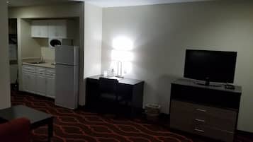 Habitación de hotel compacta con kitchenette, televisión de pantalla plana, escritorio y alfombra estampada.