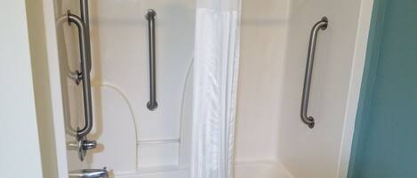 Un baño con bañera, barras de apoyo, cortina de ducha y toalla.
