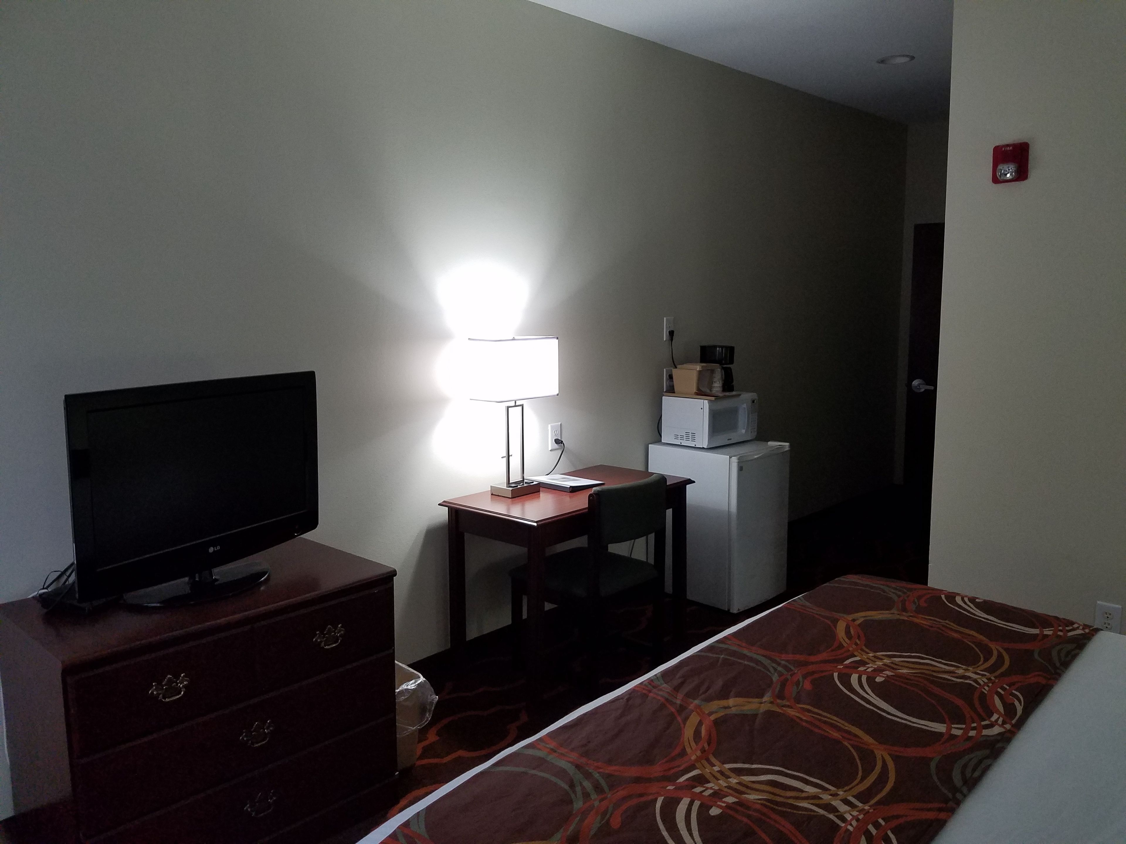 Une chambre d’hôtel équipée d’un lit, d’un bureau, d’une télévision, d’une lampe, d’un réfrigérateur et d’un four à micro-ondes.