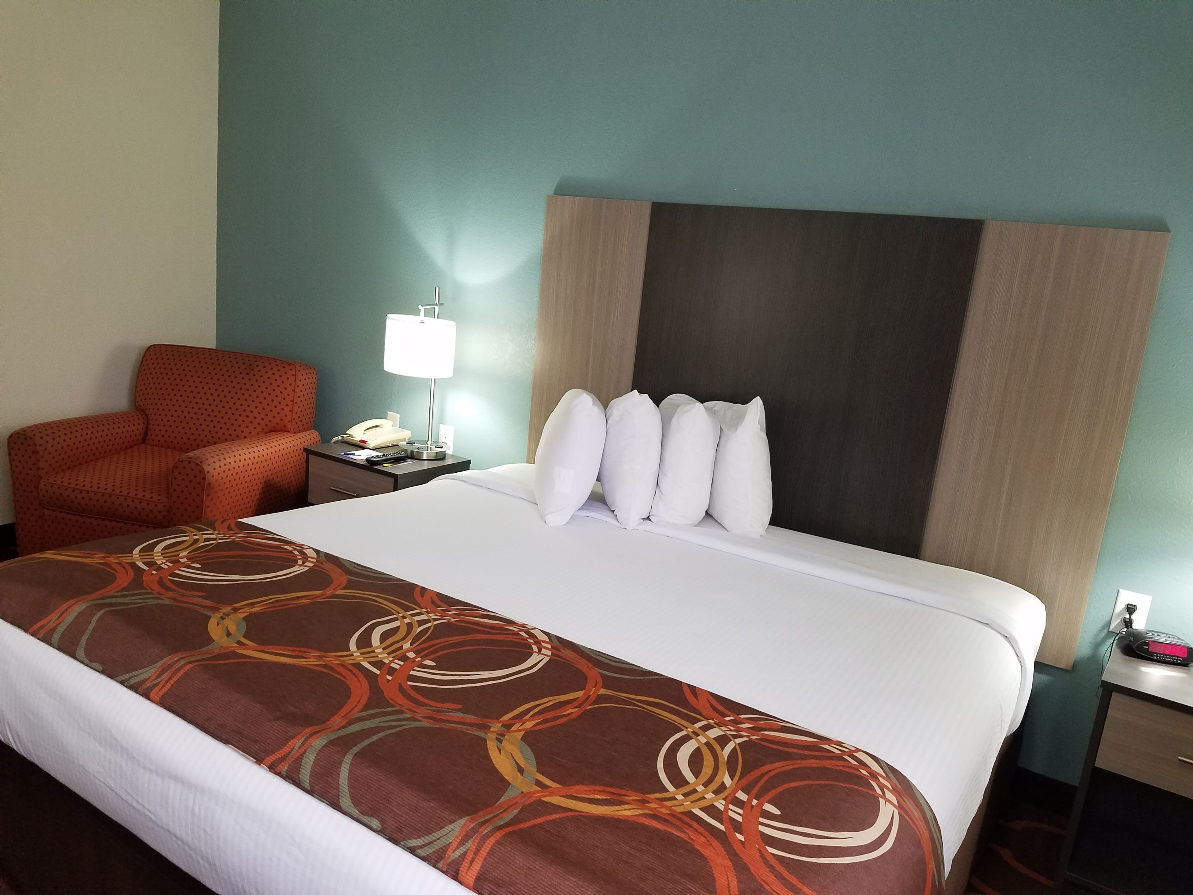 A hotel room with a bed, a nightstand with a lamp, a telephone, and a red armchair.