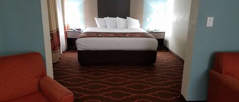 A hotel room with a large bed, two red armchairs, a ceiling fan, and a patterned carpet.