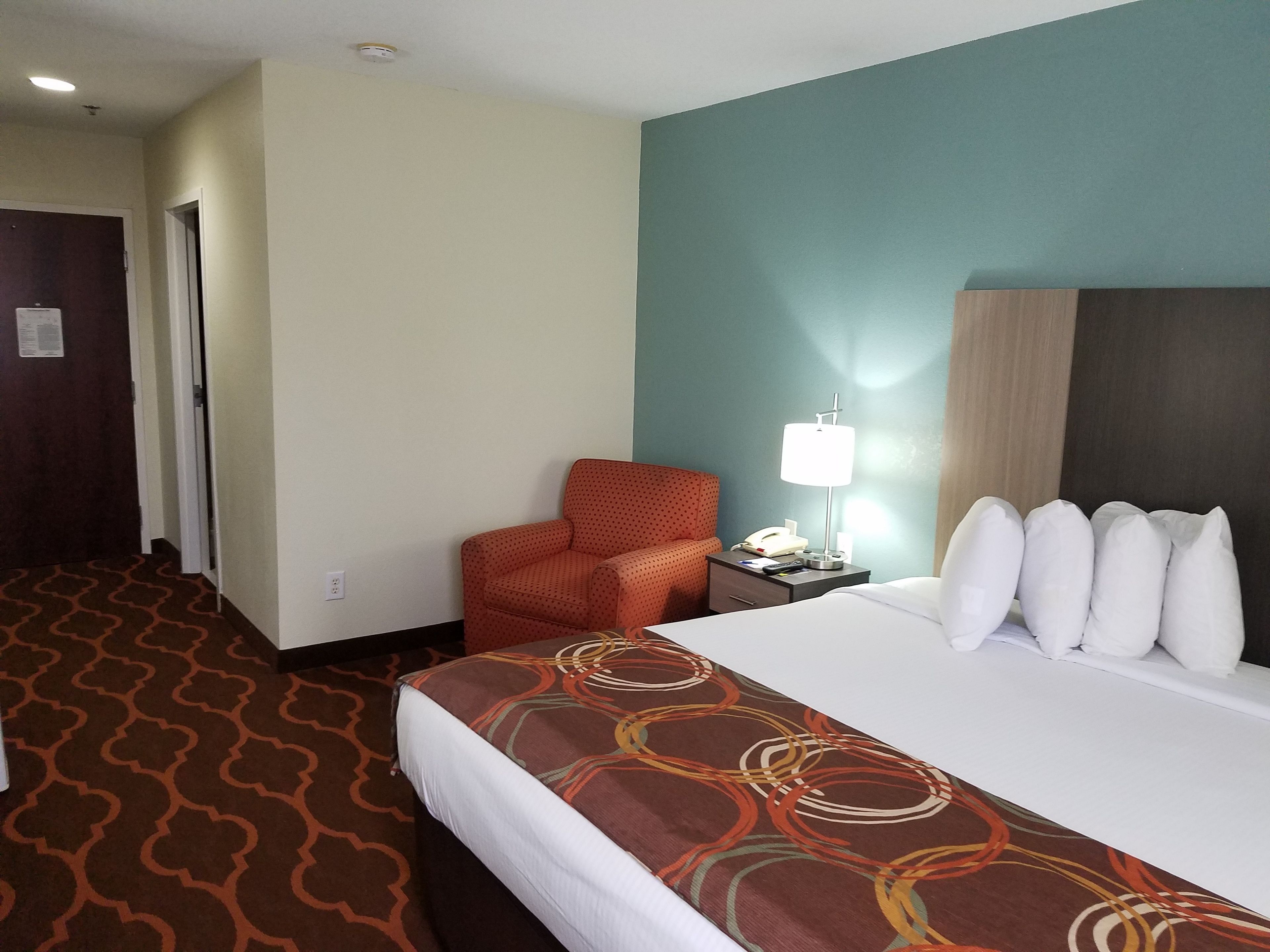 A hotel room with a bed, a chair, a nightstand with a lamp, and a telephone.