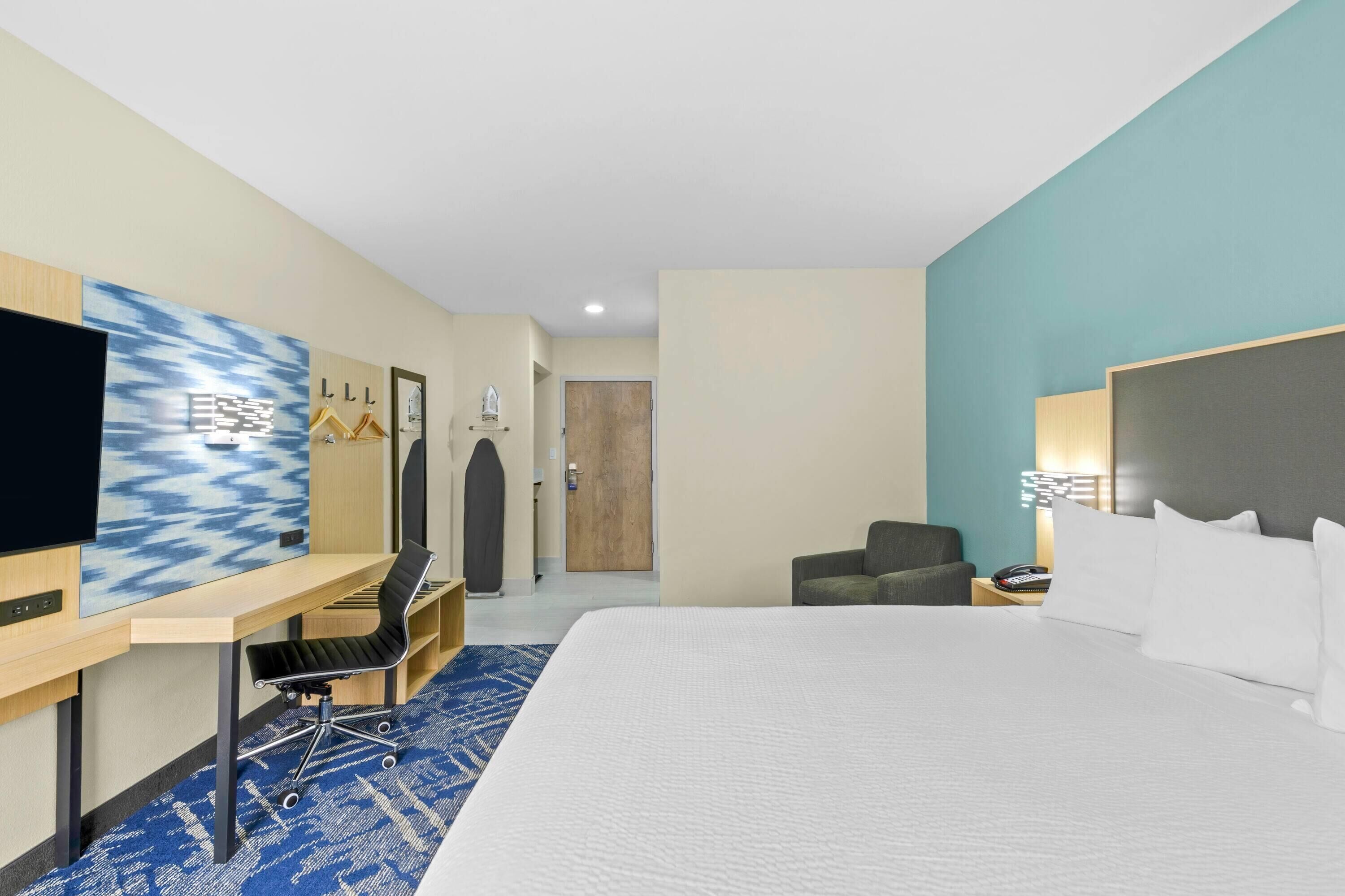 Ein Hotelzimmer mit einem großen Bett, einem Schreibtisch mit Stuhl, einem Fernseher und einem Kleiderschrank.