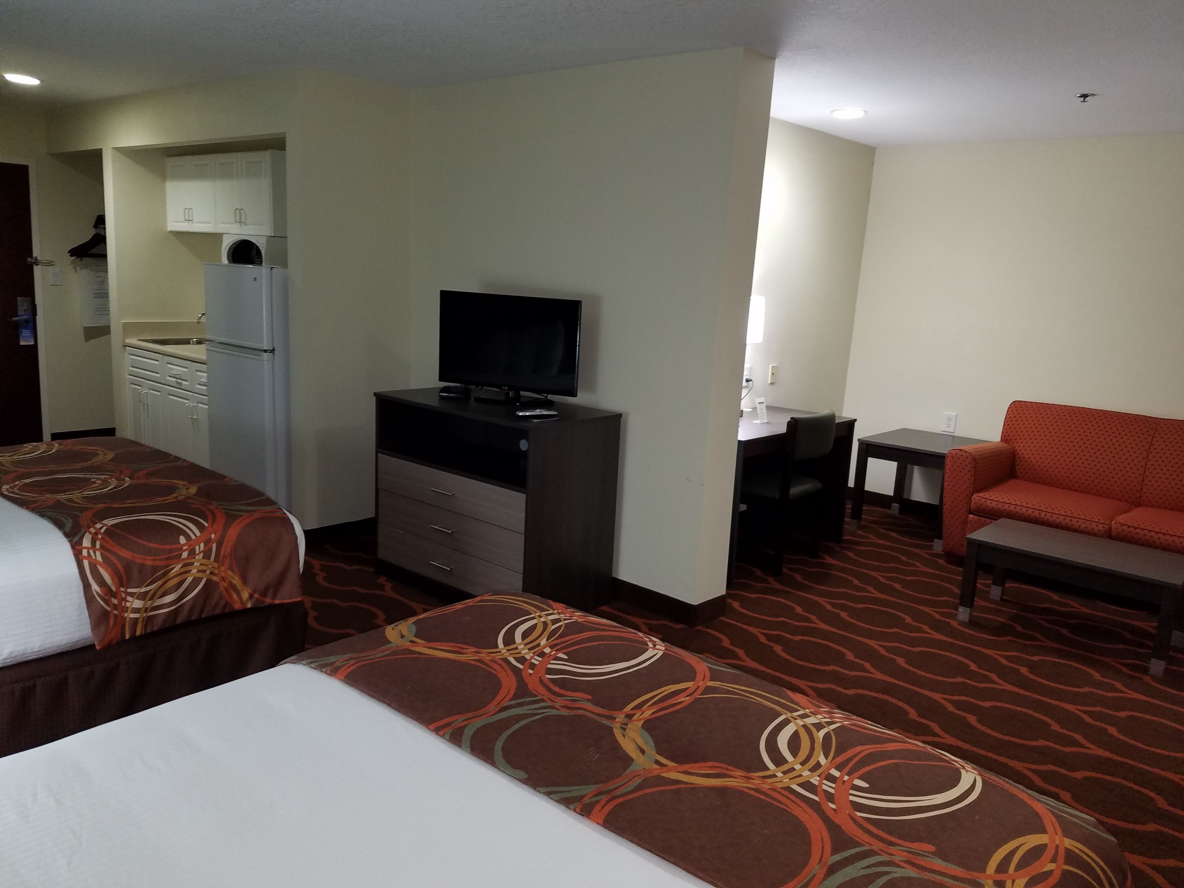 A hotel room with two beds, a desk, a television, a sofa, and a kitchenette.
