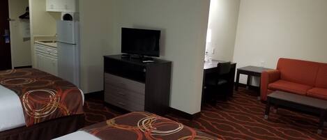 A hotel room with two beds, a desk, a television, a sofa, and a kitchenette.