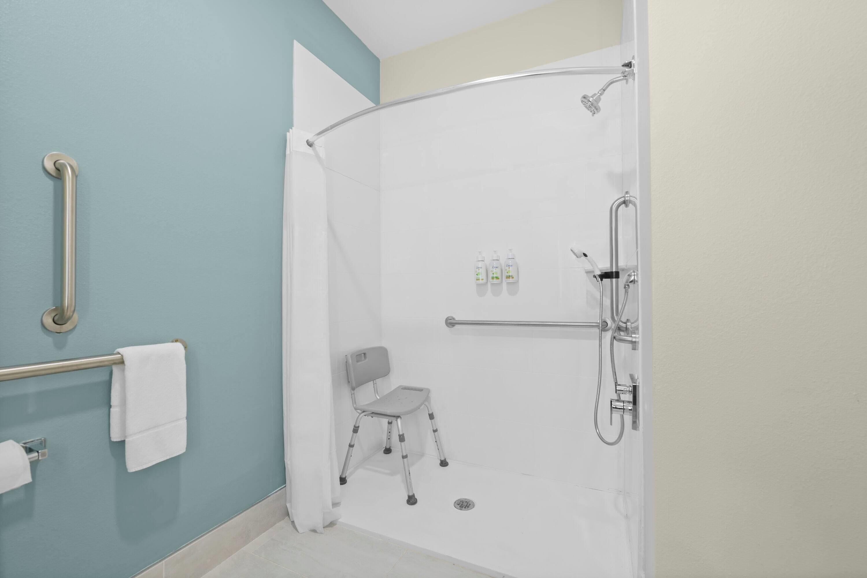 Un espace douche équipé d’une barre d’appui, d’une chaise et d’un sèche-mains.