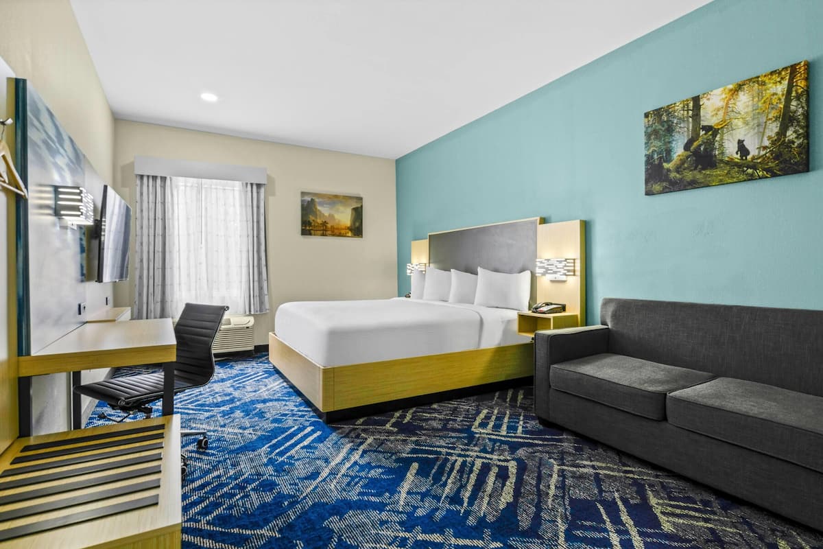 A hotel room with a bed, a desk, a chair, a sofa, and a large window with curtains.
