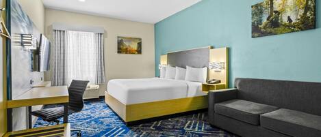 A hotel room with a bed, a desk, a chair, a sofa, and a large window.