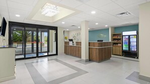 A reception area with a glass door entrance, a reception desk, a wall-mounted TV, and a beverage refrigerator. - Baymont by Wyndham Grovetown Augusta (Grovetown)