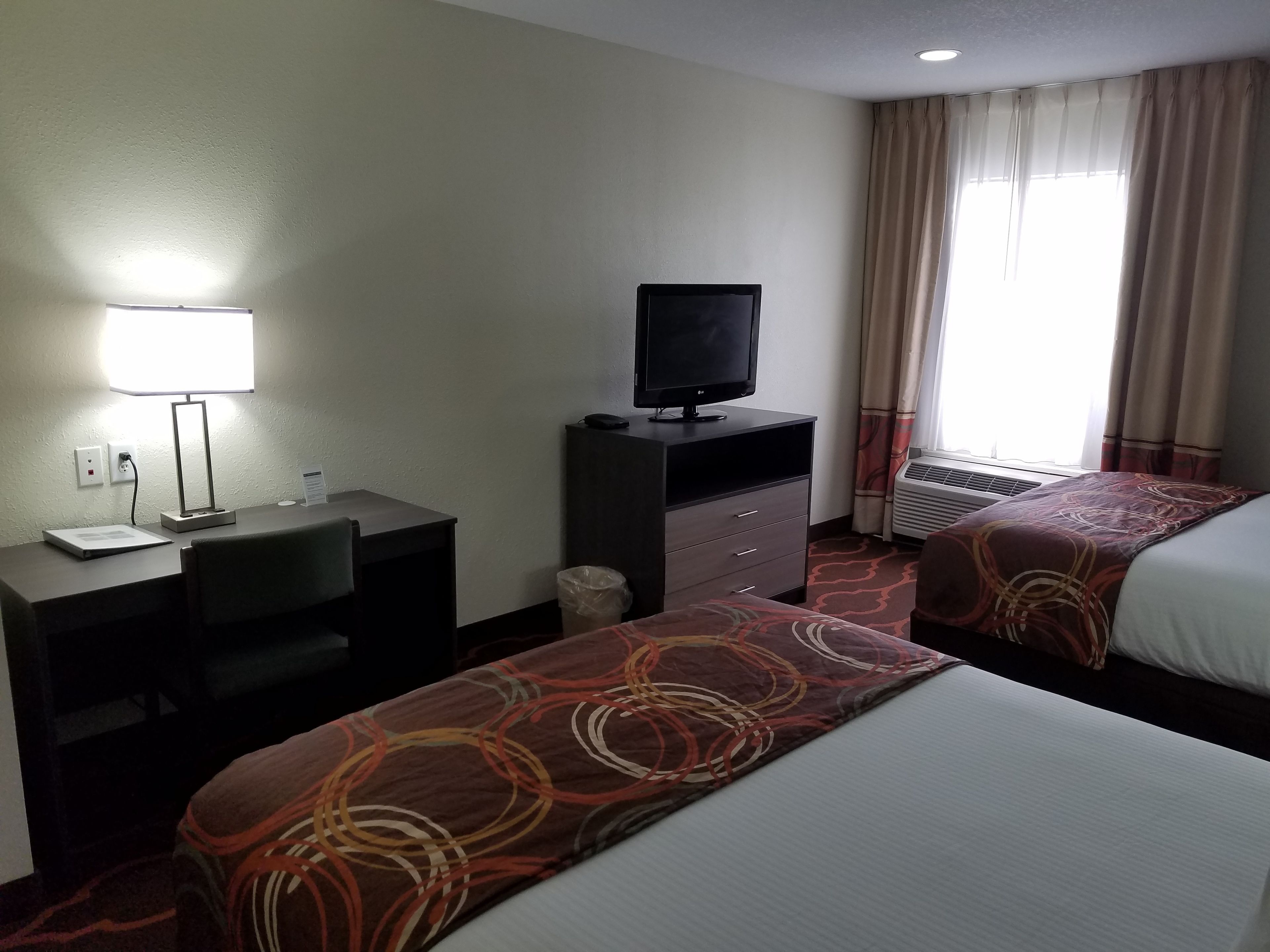 Une chambre d’hôtel équipée d’un bureau, d’une télévision, d’un lit et d’une fenêtre avec des rideaux.