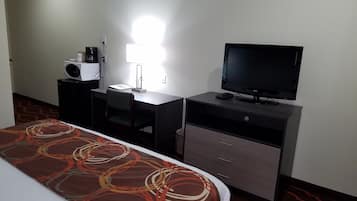 A hotel room with a bed, a desk with a computer, a television, and a lamp.