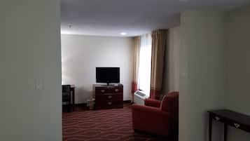 Ein Hotelzimmer mit rotem Teppich, einem Flachbildfernseher auf einer Holzkombination, einem roten Sessel und einem Fenster mit Vorhängen.