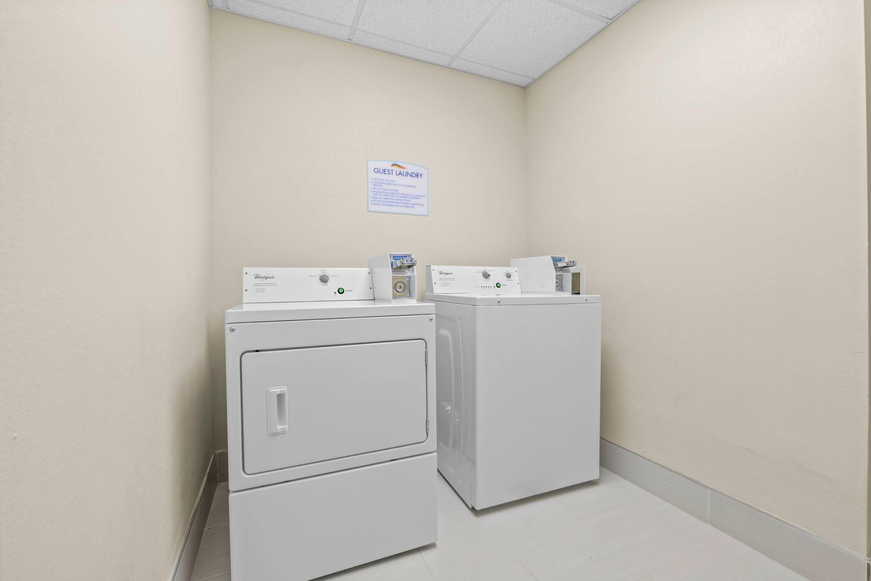 A laundry room with two Whirlpool washers and dryers, a sign indicating guest laundry, and a tiled floor.