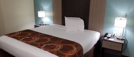 A hotel room with a large bed, two bedside tables, a desk with a lamp, and a phone.