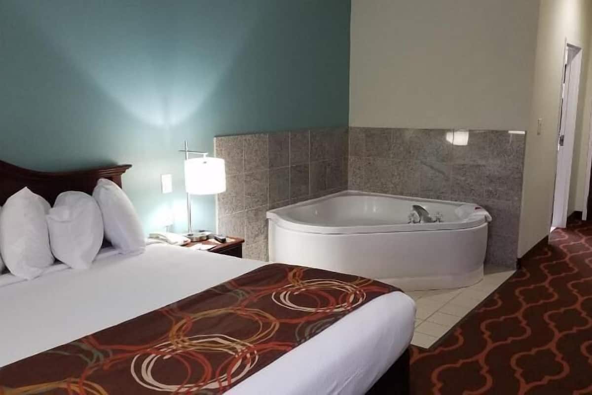 A hotel room with a bed, a large bathtub, a nightstand, and a wall-mounted lamp.