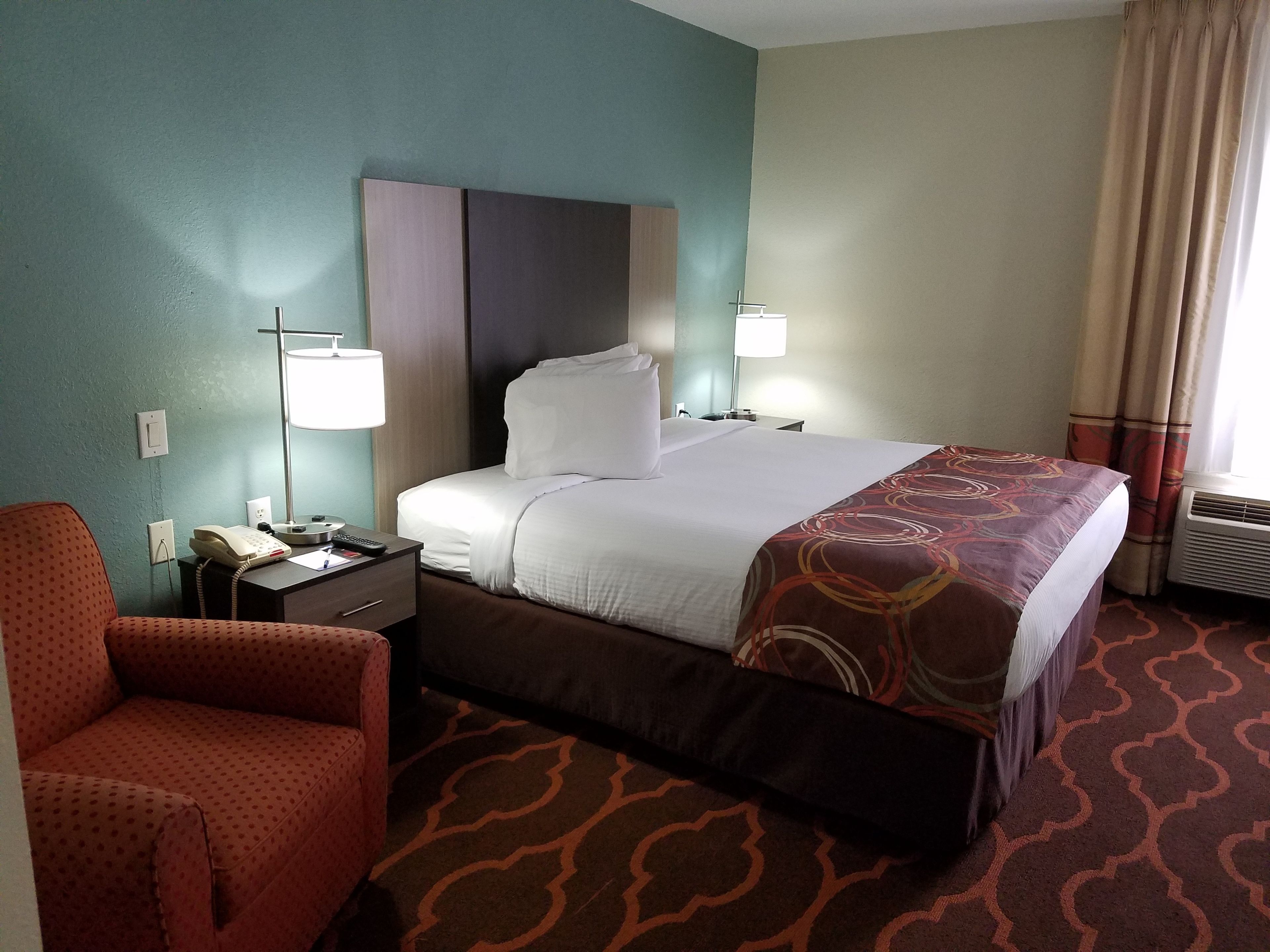 A hotel room with a bed, a desk with a telephone, a chair, and a lamp.