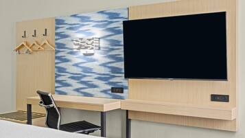 Une chambre d’hôtel comprenant un lit, un bureau avec une chaise, un téléviseur fixé au mur et un porte-manteau avec des cintres.