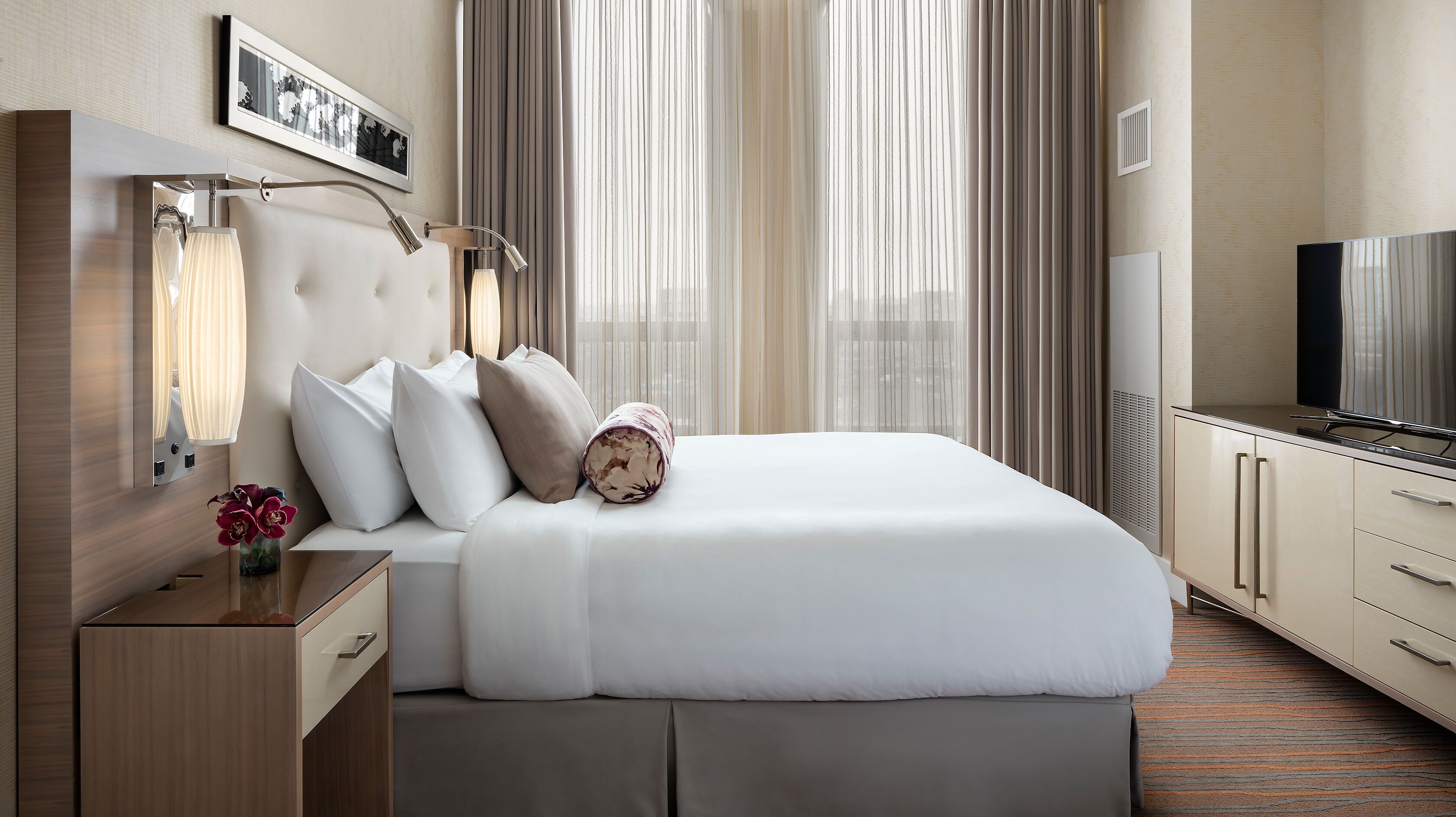 Habitación de hotel con una cama grande, televisión, escritorio con lámpara y un cuadro en la pared.