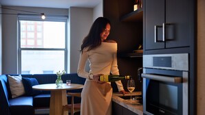 Donna versa champagne in un bicchiere in una cucina moderna con mobili scuri e forno a incasso.