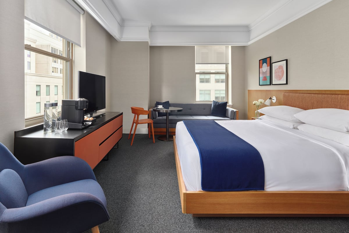 A hotel room with a bed, a desk, a chair, a TV, and a window.