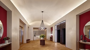 Un'ampia hall con pavimento in parquet a spina di pesce, un tavolo rotondo centrale con una pianta e un lampadario moderno.